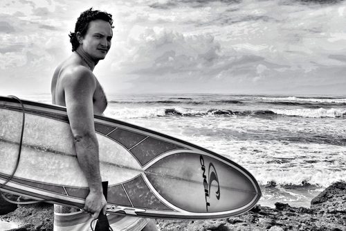 Black and white medium portrait of a surfer standing at the shoreline before entering the water