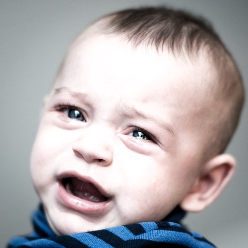 Close-up portrait of a crying baby looking directly into the camera, processed with muted, desaturated colors.